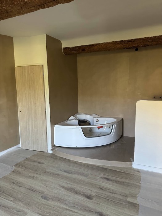 Salle de bains enduite à la chaux, baignoire d'angle sous poutre apparente