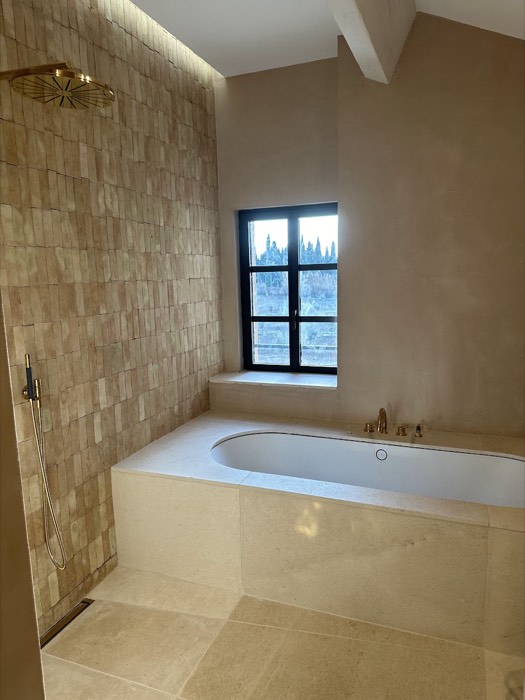 Baignoire habillée de pierre claire et pan de zelliges sous la fenêtre
